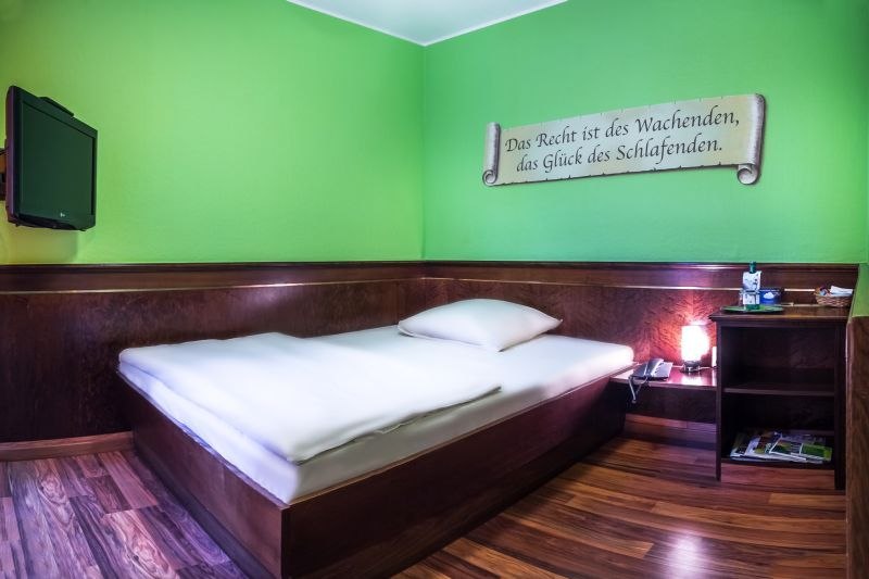Room with green-painted walls, French bed, wall quote and small bedside table with lamp., &copy; TOMAS