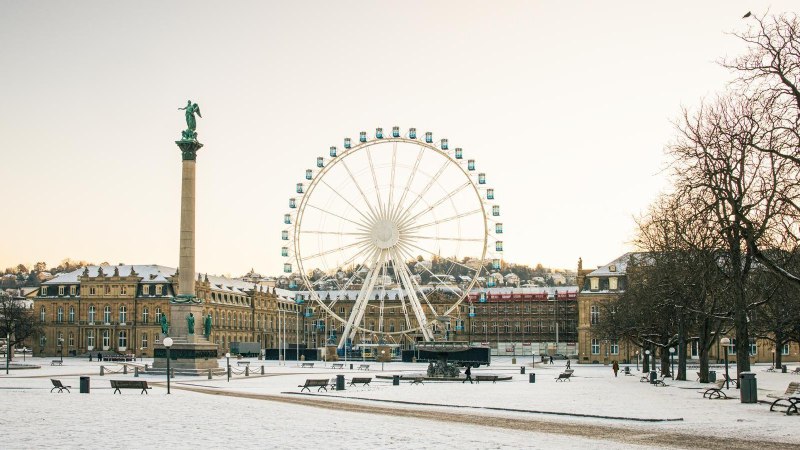 Wintery Schlossplatz in Stuttgart with snow-covered ground, a tall column and a large Ferris wheel in front of a castle in the background., &copy; Stuttgart-Marketing GmbH, Sarah Schmid