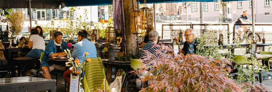Ein belebtes Caf&eacute; im Freien mit Menschen, die an Tischen unter Sonnenschirmen sitzen. Pflanzen und Dekorationen schaffen eine gem&uuml;tliche Atmosph&auml;re., &copy; SMG Stuttgart Marketing GmbH - Sarah Schmid
