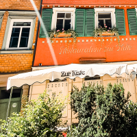 The Zur Kiste wine bar with its red façade, green shutters and awning. Plants adorn the entrance area., © Stuttgart-Marketing GmbH