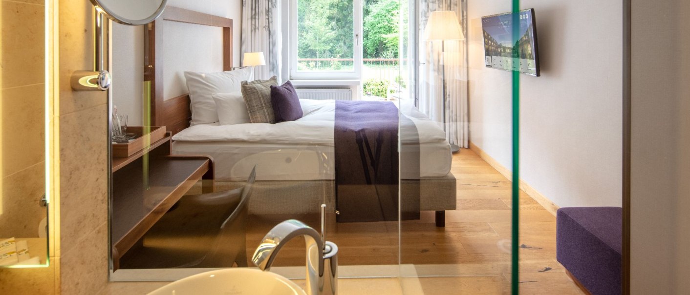Modern single room with large bed, TV and open bathroom. Bright furnishings with wooden floor and view of the countryside., &copy; Waldhotel Stuttgart GmbH
