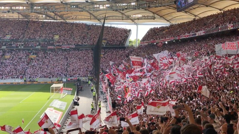 Blick in die Cannstatter Kurve der Mercedes-Benz Arena Stuttgart. Fans schwenken rot-wei&szlig;e Fahnen und halten Banner hoch. Die Trib&uuml;nen sind voll besetzt., &copy; Stuttgart-Marketing GmbH