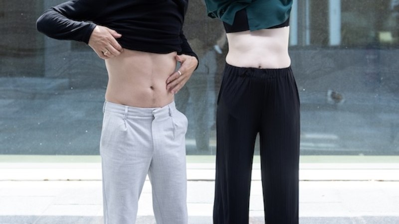 Zwei Personen heben ihre Oberteile und zeigen ihre B&auml;uche. Sie stehen vor einem modernen Geb&auml;ude mit Glasfassade., &copy; Renitenztheater Stuttgart e.V.