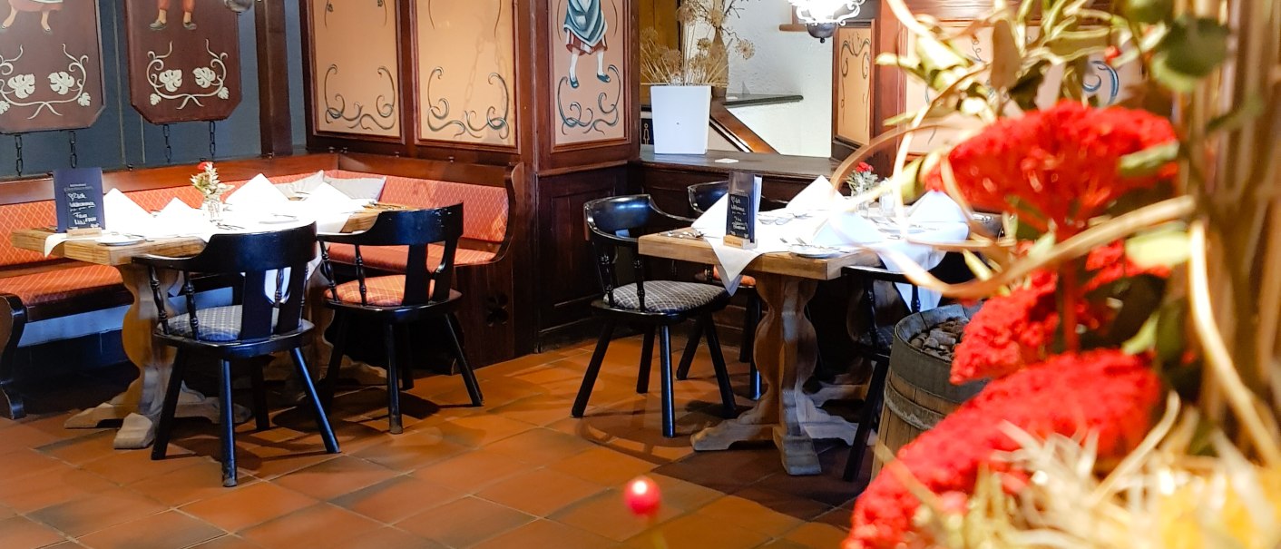 Gemütliches Restaurant mit Holzmöbeln, dekorativen Wandmalereien und roten Blumen im Vordergrund. Die Tische sind mit weißen Servietten gedeckt., © ©hotel-graf-eberhard.de