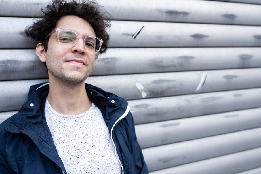 Ein Mann mit lockigem Haar und Brille lehnt l&auml;ssig an einer grauen, metallischen Wand., &copy; Julia Sch&auml;fer