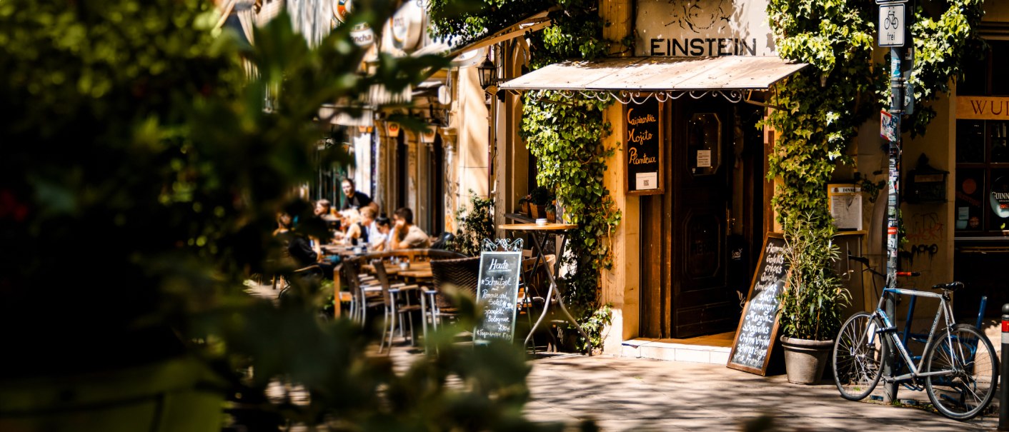 Ein gemütliches Café namens Einstein mit Pflanzen und Fahrrädern. Menschen sitzen draußen und genießen das Wetter., © SMG Stuttgart Marketing GmbH - Sarah Schmid