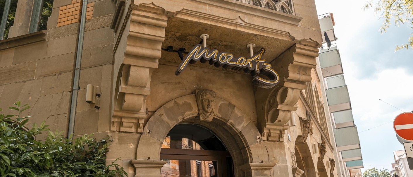 Eingang eines historischen Gebäudes mit dem Schriftzug 'Mozart3' über dem Torbogen. Verzierungen und Pflanzen sind sichtbar., © SMG, Sarah Schmid