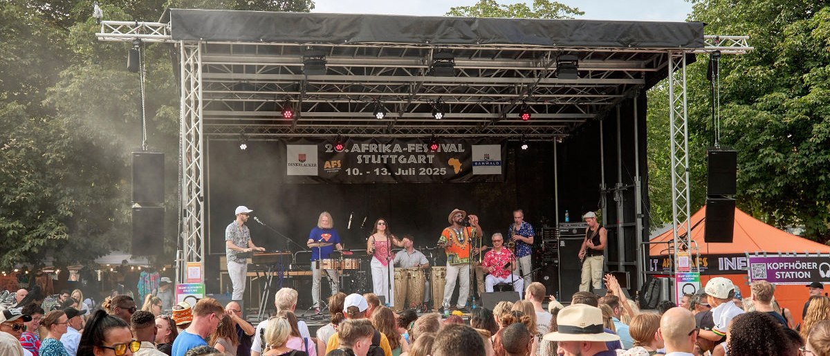 Eine Band performt auf der Bühne des Afrika-Festivals Stuttgart 2025. Viele Zuschauer genießen die Musik bei sonnigem Wetter., © Afrika-Festival Stuttgart e.V. Eine Band performt auf der Bühne des Afrika-Festivals Stuttgart 2025. Viele Zuschauer genießen die Musik bei sonnigem Wetter., © Afrika-Festival Stuttgart e.V.
