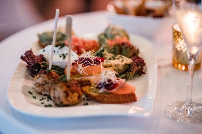Ein Teller mit verschiedenen Vorspeisen, darunter Brot mit Lachs und Fleischb&auml;llchen, auf einem Tisch mit einem Glas Sekt., &copy; Cool-Tours StattReisen