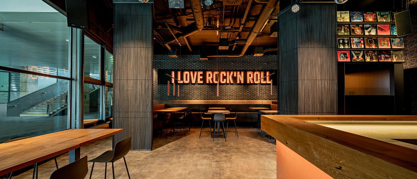 Ein Café mit moderner Einrichtung, beleuchtetem "I Love Rock'n'Roll"-Schild und Plattencovern an der Wand. Holztische und Stühle sind zu sehen., © Maks Richter