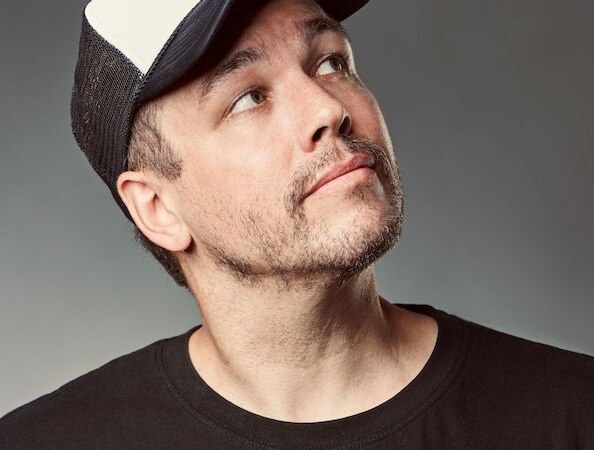A man in a black T-shirt and a two-tone baseball cap looks upwards. The background is neutral., &copy; Rosenau Kultur e.V.