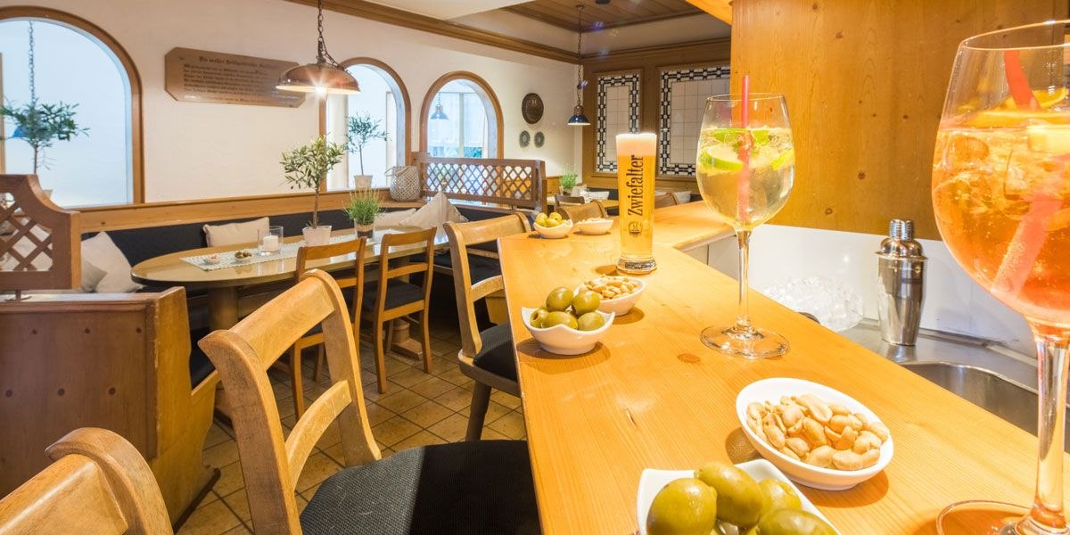 Gemütliche Bar mit Holzmöbeln, Getränken und Snacks. Ein Glas Bier und Cocktails stehen auf der Theke, umgeben von Oliven und Nüssen., © Best Western Plus Hotel am Schlossberg