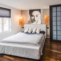 Modernes Hotelzimmer mit gro&szlig;em Bett, Wandbild einer Frau, zwei H&auml;ngelampen und Holzfu&szlig;boden., &copy; Zauberlehrling