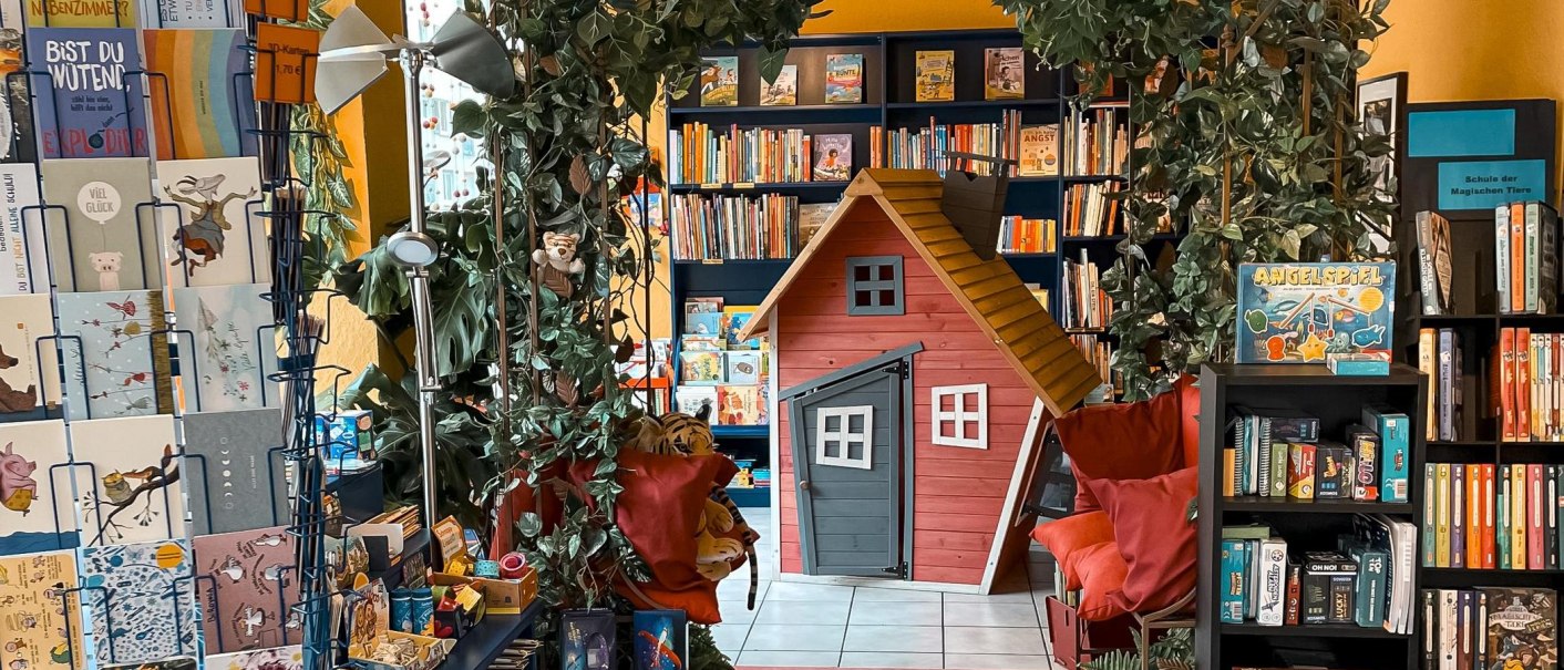 Buchladen mit Spielhaus, Pflanzen und Regalen voller Bücher und Spiele. Bunte Postkarten und Spiele sind ebenfalls ausgestellt., © Naseweis, Stuttgart