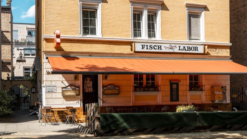 A restaurant called Fischlabor with an orange awning and outdoor seating. The building has yellow brick walls and white window frames., © SMG Stuttgart Marketing GmbH - Sarah Schmid