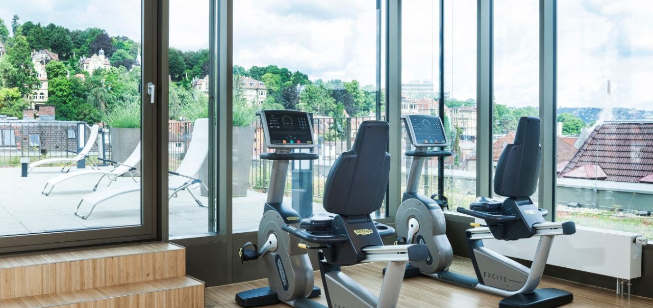 Fitnessraum mit zwei Fahrradergometern, großen Fenstern und Blick auf eine Terrasse mit Liegestühlen und grüner Landschaft., © Park Inn by Radisson Stuttgart Fitnessraum mit zwei Fahrradergometern, großen Fenstern und Blick auf eine Terrasse mit Liegestühlen und grüner Landschaft., © Park Inn by Radisson Stuttgart