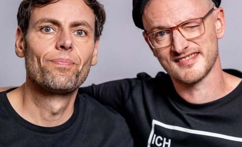 Zwei M&auml;nner in schwarzen T-Shirts, einer tr&auml;gt eine M&uuml;tze und zwinkert. Sie posieren vor einem neutralen Hintergrund., &copy; Rosenau Kultur e.V.