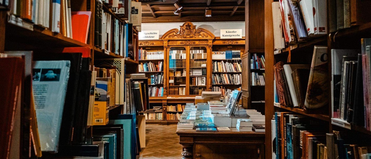 Ein gemütliches Antiquariat mit hohen Bücherregalen und einem Tisch voller Bücher. Im Hintergrund sind kunstvoll verzierte Holzregale zu sehen., © Stuttgart-Marketing GmbH, Sarah Schmid Ein gemütliches Antiquariat mit hohen Bücherregalen und einem Tisch voller Bücher. Im Hintergrund sind kunstvoll verzierte Holzregale zu sehen., © Stuttgart-Marketing GmbH, Sarah Schmid