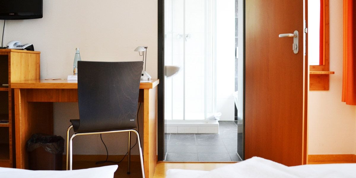 A hotel room with a desk, chair and view of the bathroom. A water bottle and lamp are on the table., &copy; ECOINN Hotel am Campus