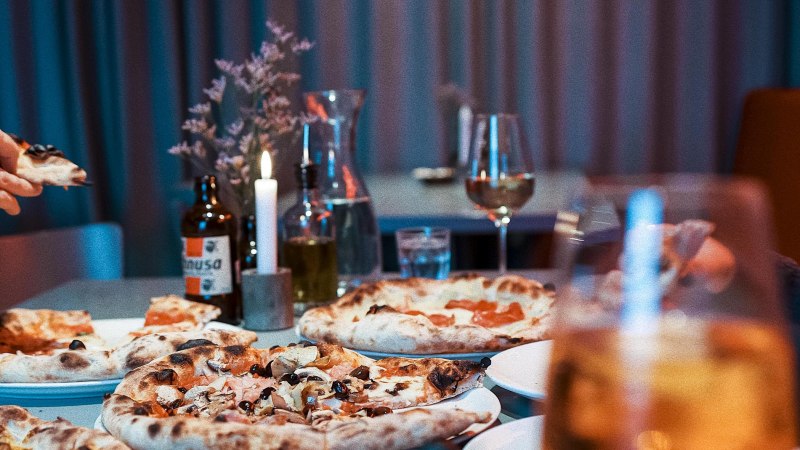 Ein Tisch in einem Restaurant mit mehreren Pizzen, Getr&auml;nken und einer brennenden Kerze. Im Hintergrund sind Gl&auml;ser und eine Flasche zu sehen., &copy; Italo Disco, Stuttgart