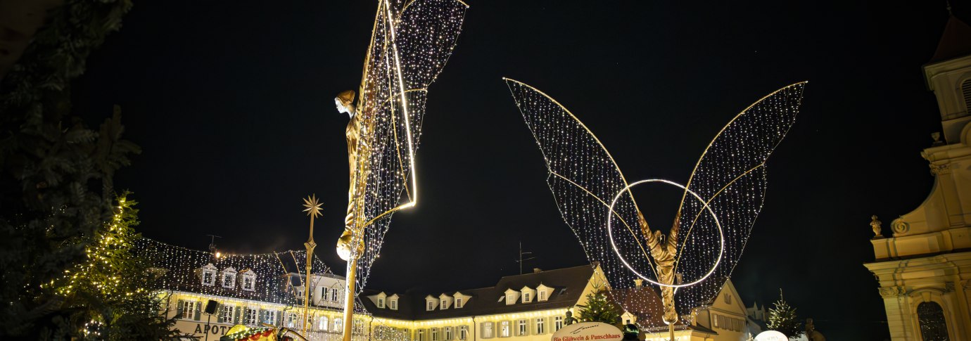 Der Ludwigsburger Barock-Weihnachtsmarkt auf dem Marktplatz bei Nacht, beleuchtete gro&szlig;e Engelsfiguren und Buden. Einige Besucherinnen und Besucher tummeln sich auf dem Platz., &copy; Stuttgart Marketing GmbH, Sarah Schmid