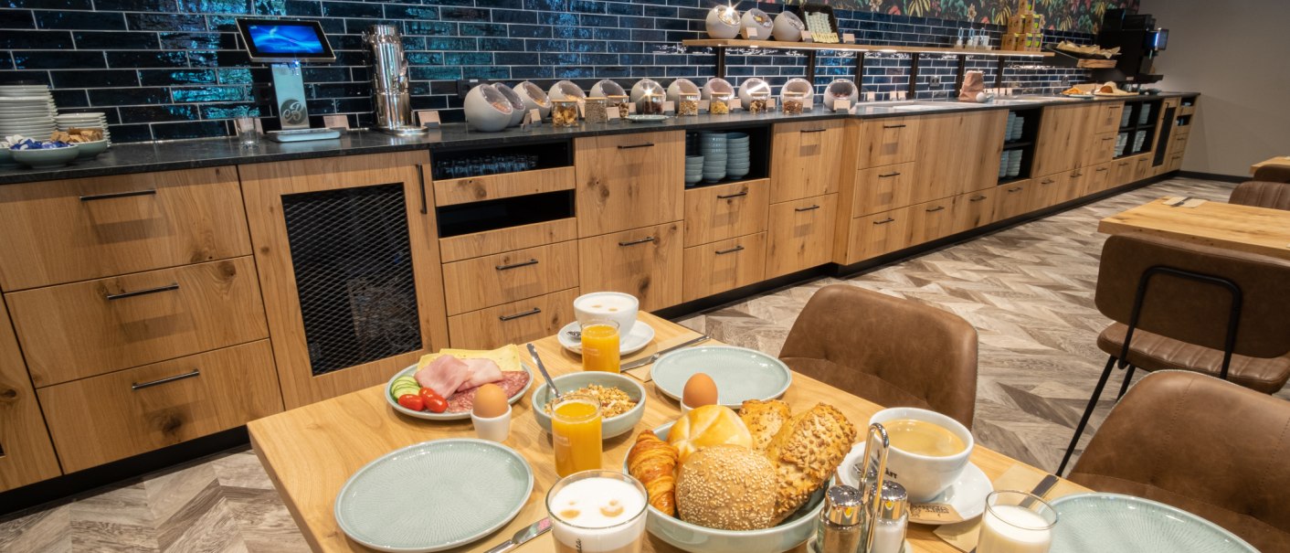 Ein reichhaltiges Fr&uuml;hst&uuml;cksbuffet mit Br&ouml;tchen, Croissants, Aufschnitt, Eiern und Getr&auml;nken auf einem Tisch vor einer modernen Buffet-Theke., &copy; 13 6 Design GmbH (Judenhof 10, 89073 Ulm)