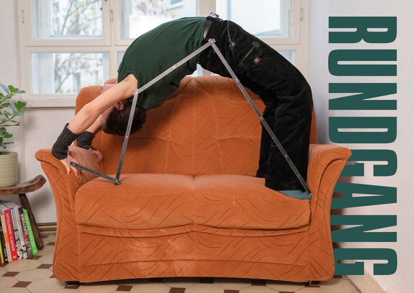 Eine Person macht eine Brücke auf einem orangefarbenen Sofa, unterstützt von einem Metallgestell. Im Hintergrund sind Fenster und Pflanzen zu sehen., © Merz Akademie Eine Person macht eine Brücke auf einem orangefarbenen Sofa, unterstützt von einem Metallgestell. Im Hintergrund sind Fenster und Pflanzen zu sehen., © Merz Akademie