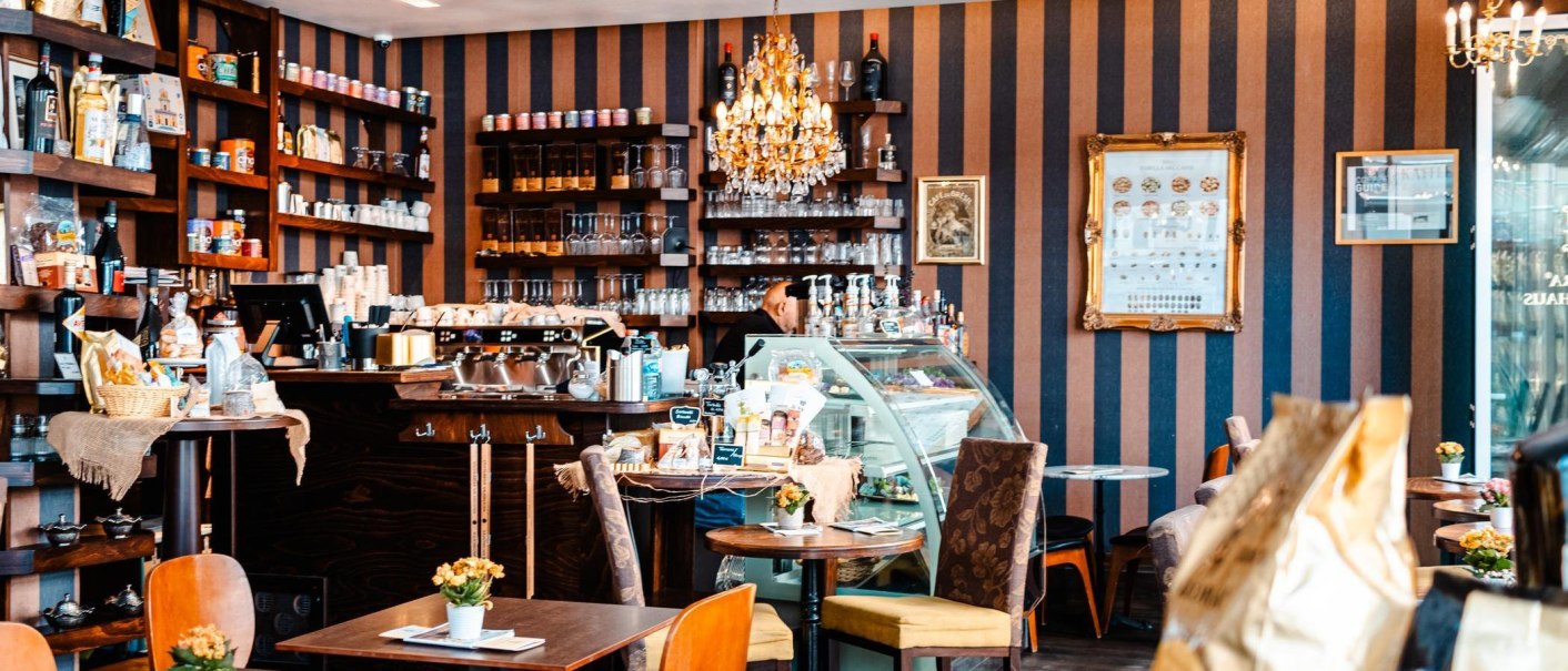 Gemütliches Kaffeehaus mit Kronleuchter, Regalen voller Produkte und einer Theke mit Kaffeemaschine. Tische mit Blumen dekoriert., © Stuttgart-Marketing GmbH, Sarah Schmid
