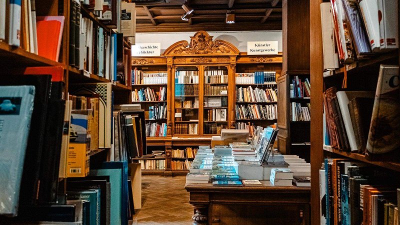 Ein gemütliches Antiquariat mit hohen Bücherregalen und einem Tisch voller Bücher. Im Hintergrund sind kunstvoll verzierte Holzregale zu sehen., © Stuttgart-Marketing GmbH, Sarah Schmid Ein gemütliches Antiquariat mit hohen Bücherregalen und einem Tisch voller Bücher. Im Hintergrund sind kunstvoll verzierte Holzregale zu sehen., © Stuttgart-Marketing GmbH, Sarah Schmid