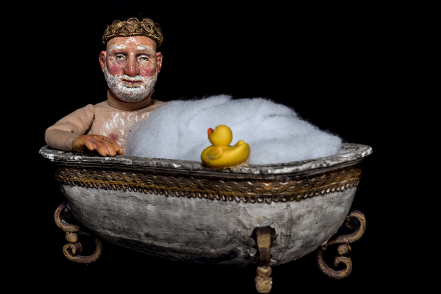 Eine Figur mit Krone sitzt in einer antiken Badewanne voller Schaum, neben einer gelben Gummiente., © Schäfer & Thieme Produktion Eine Figur mit Krone sitzt in einer antiken Badewanne voller Schaum, neben einer gelben Gummiente., © Schäfer & Thieme Produktion