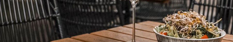 A glass of white wine, a plate of pasta and a salad on a wooden table in a restaurant with woven chairs., © SMG, itchyfeet-travel.de