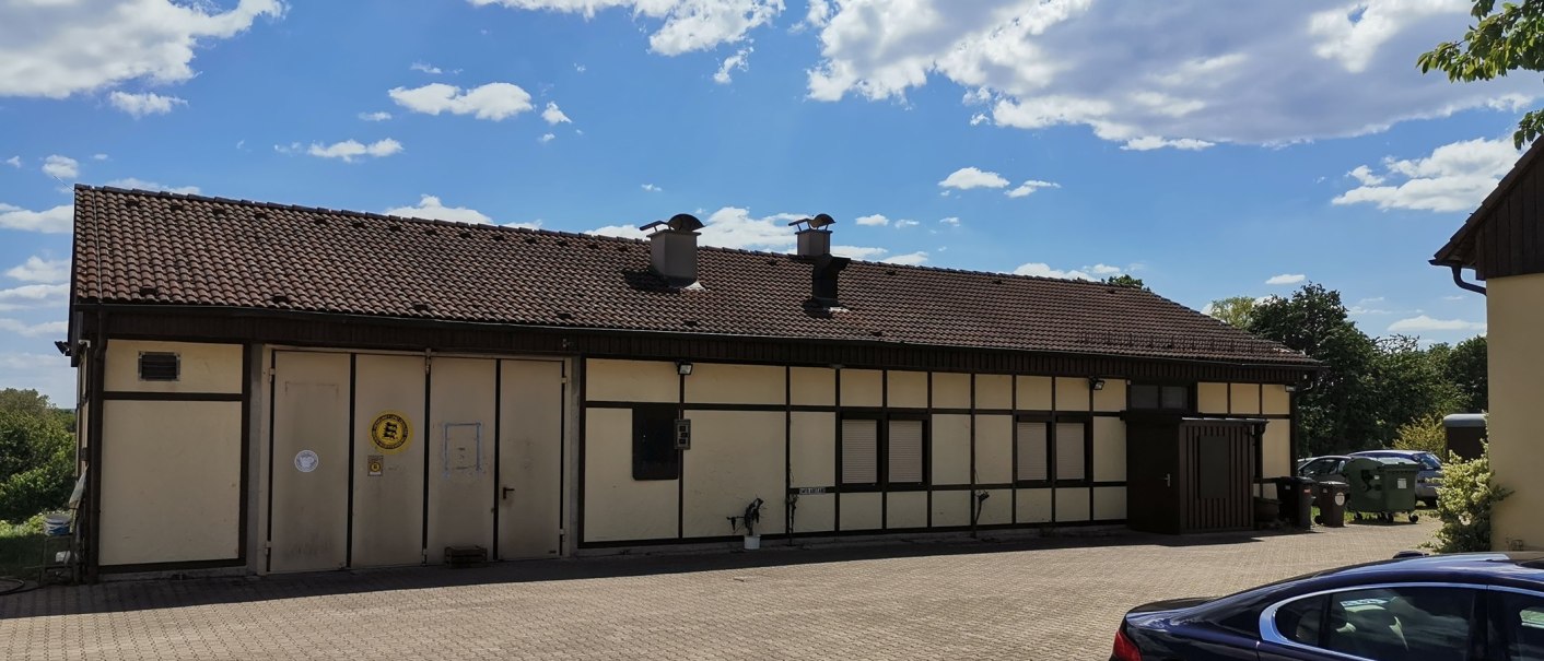 Half-timbered building with a tiled roof and chimneys, surrounded by trees and cars. The sky is blue with a few clouds., © Weinbau Glock und Sohn GbR