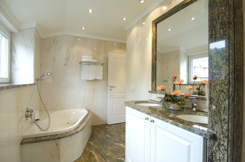 An elegant bathroom featuring a whirlpool tub, double sinks, marble walls, and a floral arrangement. Bright lighting and windows create a pleasant atmosphere., © Jeanette Bender An elegant bathroom featuring a whirlpool tub, double sinks, marble walls, and a floral arrangement. Bright lighting and windows create a pleasant atmosphere., © Jeanette Bender
