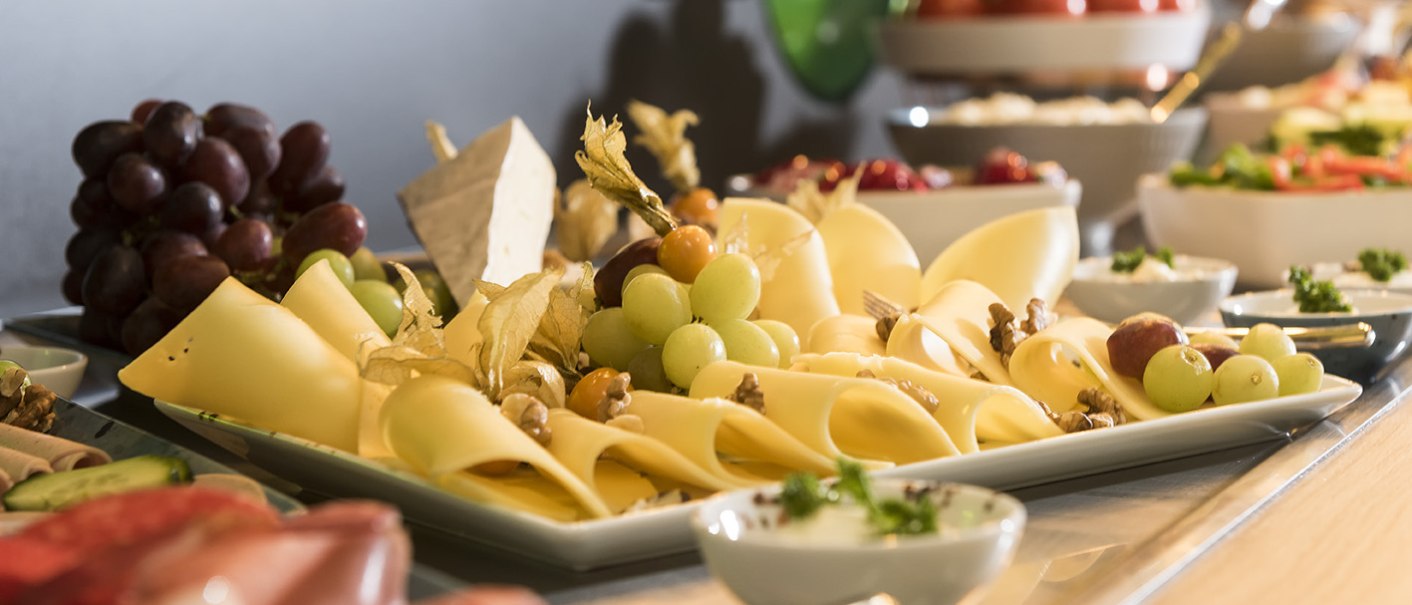 Ein reichhaltiges Frühstücksbuffet mit Käse, Trauben, Tomaten und weiteren Speisen auf einem Tisch arrangiert., © ibis Styles Stuttgart Vaihingen
