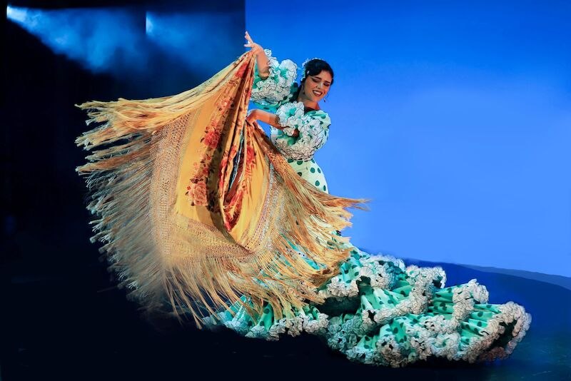 Eine Flamenco-T&auml;nzerin in einem gr&uuml;nen Kleid mit wei&szlig;en Punkten und Fransen tanzt leidenschaftlich auf einer B&uuml;hne mit blauem Hintergrund., &copy; Stuttgarter Flamenco Festival gUG