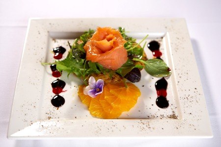 Gourmet-Vorspeise mit Lachs, Orangen, Salat und essbarer Blüte, kunstvoll auf einem weißen Teller angerichtet., © Jeanette Bender