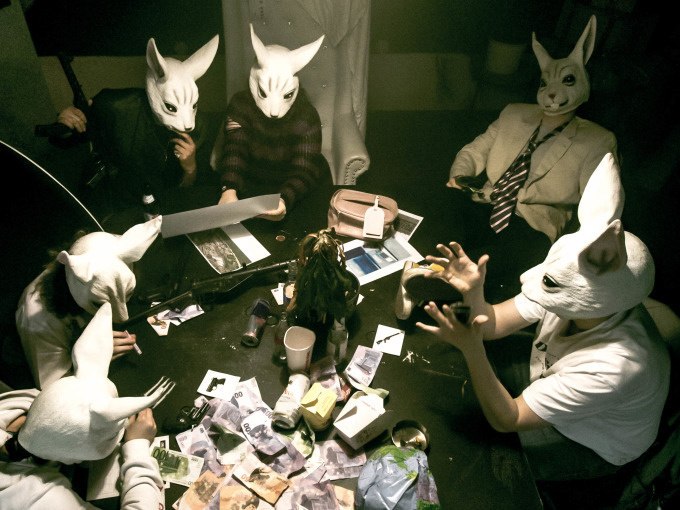 People wearing rabbit masks sit at a table full of banknotes and documents in a dark room., © ExitGames Stuttgart People wearing rabbit masks sit at a table full of banknotes and documents in a dark room., © ExitGames Stuttgart