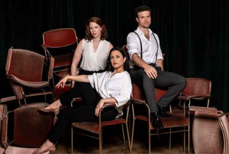 Three people in elegant clothes pose on stacked red chairs in front of a dark curtain., &copy; Internationale Hugo-Wolf-Akademie