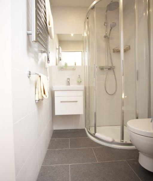 Modern bathroom with glass shower, white washbasin and toilet. Towels hang on a radiator., © Hotel Reinhardtshof Garni Modern bathroom with glass shower, white washbasin and toilet. Towels hang on a radiator., © Hotel Reinhardtshof Garni