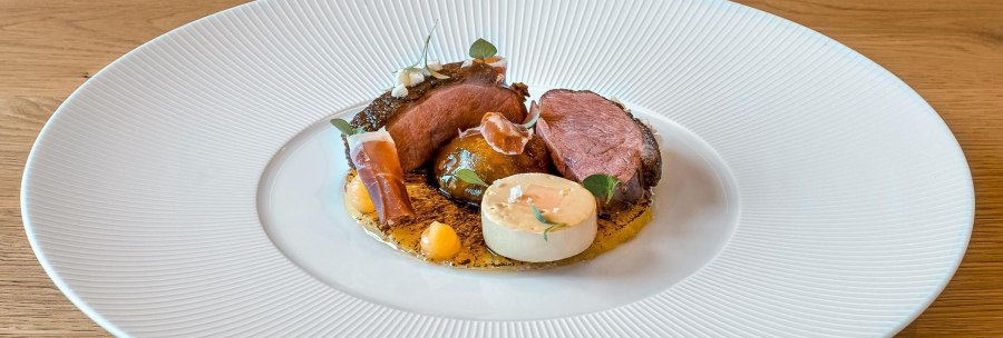 Gourmetgericht mit Entenbrust, dekorativ angerichtet auf einem weißen Teller. Beilagen und Soßen kunstvoll platziert, auf einem Holztisch serviert., © New Josch, Stuttgart Gourmetgericht mit Entenbrust, dekorativ angerichtet auf einem weißen Teller. Beilagen und Soßen kunstvoll platziert, auf einem Holztisch serviert., © New Josch, Stuttgart