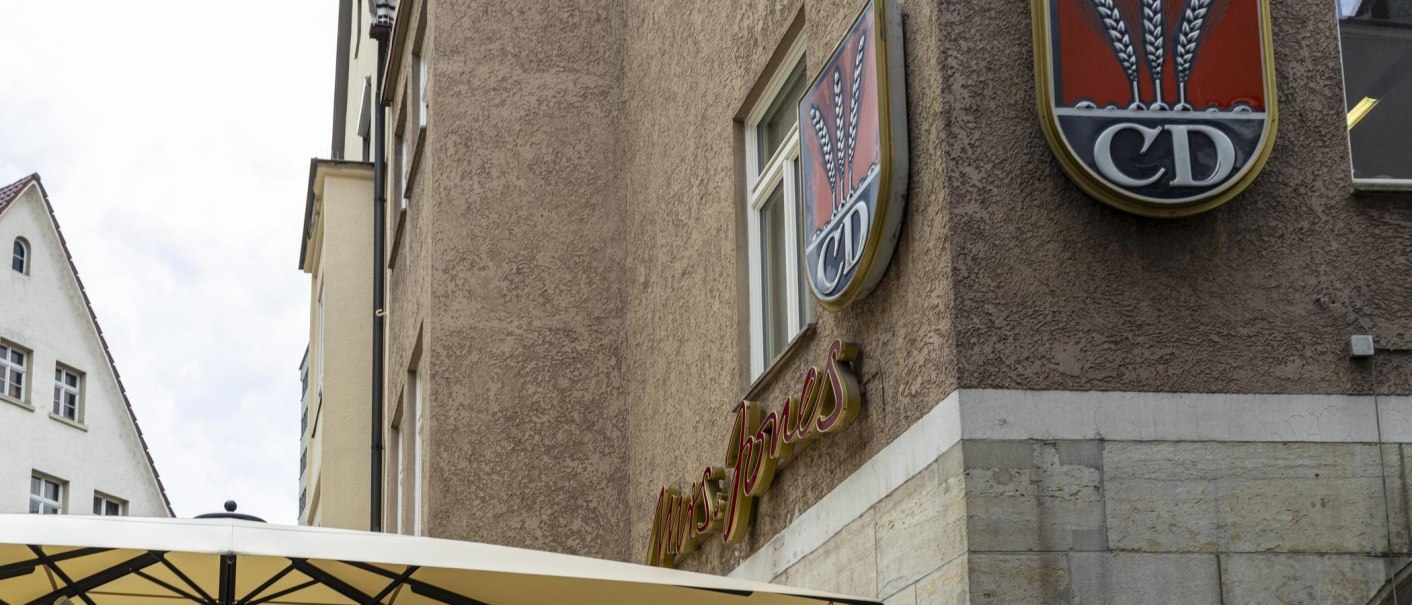 A building with the lettering 'Mrs Jones' and a logo with ears of corn and the letters 'CD'. A parasol is visible in the foreground., &copy; SMG, Sarah Schmid