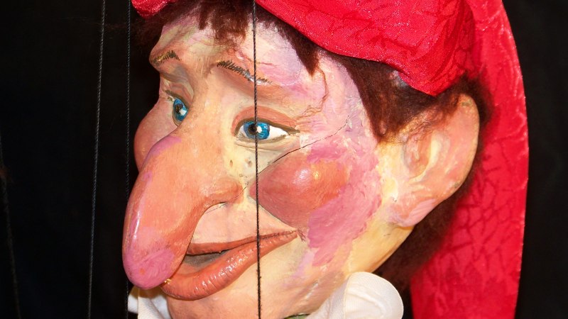 Nahaufnahme einer Kasperle-Puppe mit roter M&uuml;tze, gro&szlig;en blauen Augen und markanter Nase. Der Hintergrund ist dunkel., &copy; Nellys Puppentheater