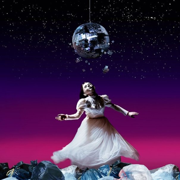 Frau in weißem Kleid tanzt unter zerbrochener Discokugel, umgeben von Müllsäcken, vor violettem Himmel., © Theaterhaus Stuttgart e.V.