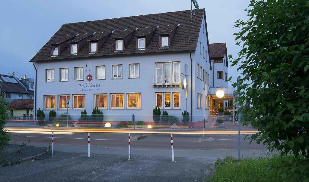 A hotel with illuminated windows at dusk. Cars drive past, creating light trails. The building has a pitched roof and several floors., © Nödinger Gastro GmbH