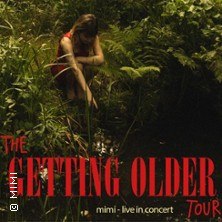 Eine Frau in einem roten Kleid sitzt nachdenklich in einem dichten Wald neben einem Bach. Der Text "The Getting Older Tour" ist prominent zu sehen., &copy; links im Bild