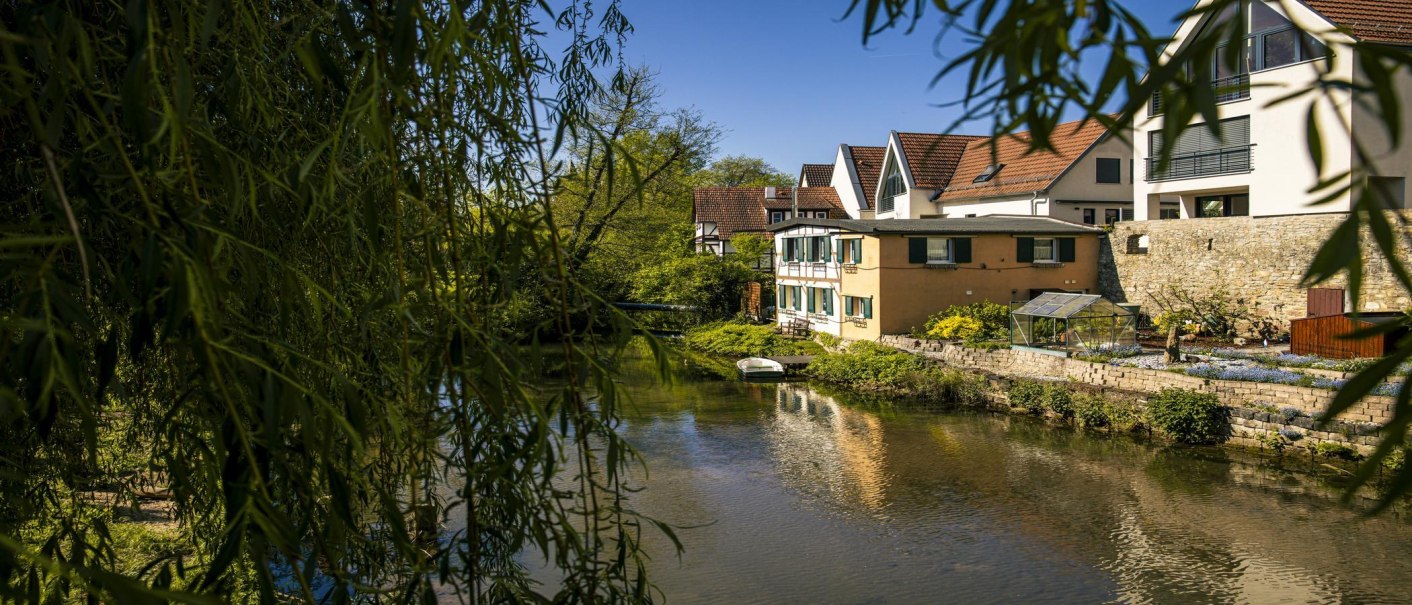 View of the banks of the Rems in Waiblingen with houses and lush greenery. A boat lies on the water, surrounded by trees and plants., © SMG Stuttgart Marketing GmbH - Sarah Schmid