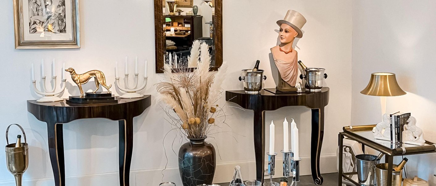 Elegante Einrichtung mit Büste, goldener Hundeskulptur, Kerzenhaltern und Spiegel. Dekorative Elemente auf Tischen und Regalen., © Metropolis Art Deco, Stuttgart