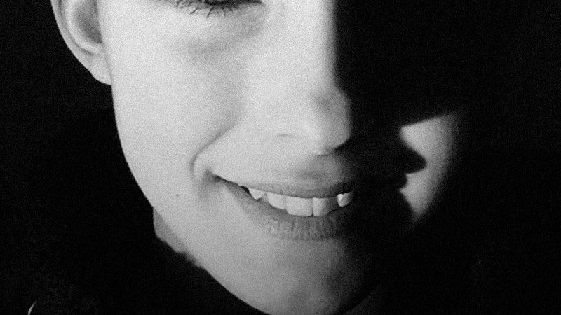 A black and white portrait of a smiling face, half of which is in shadow. An earring is visible., &copy; Theater der Altstadt