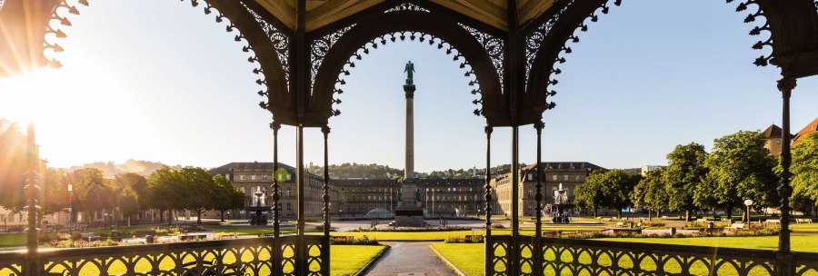 Blick durch einen Pavillon auf den Schlossplatz Stuttgart mit der Jubiläumssäule, umgeben von historischen Gebäuden und grünen Rasenflächen im Sonnenlicht., © Stuttgart-Marketing GmbH Werner Dieterich