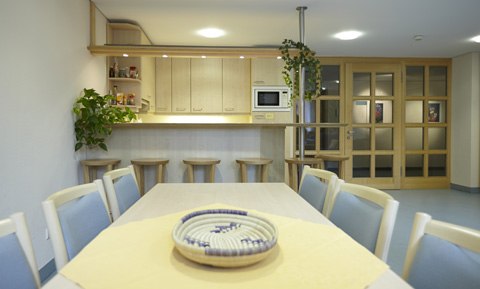 Ein heller Aufenthaltsraum mit Küche, Barhockern und Esstisch. Pflanzen und ein Korb auf dem Tisch sorgen für eine gemütliche Atmosphäre., © Ev. Diakonissenanstalt Stuttgart Ein heller Aufenthaltsraum mit Küche, Barhockern und Esstisch. Pflanzen und ein Korb auf dem Tisch sorgen für eine gemütliche Atmosphäre., © Ev. Diakonissenanstalt Stuttgart